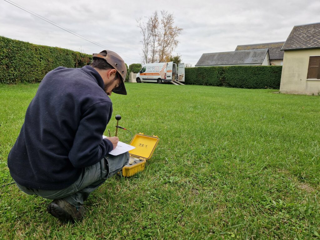Technicien réalisant une étude de sol sur un terrain constructible avant un projet de construction avec Maisons Caen Construction. Analyse du sol et prise de mesures.