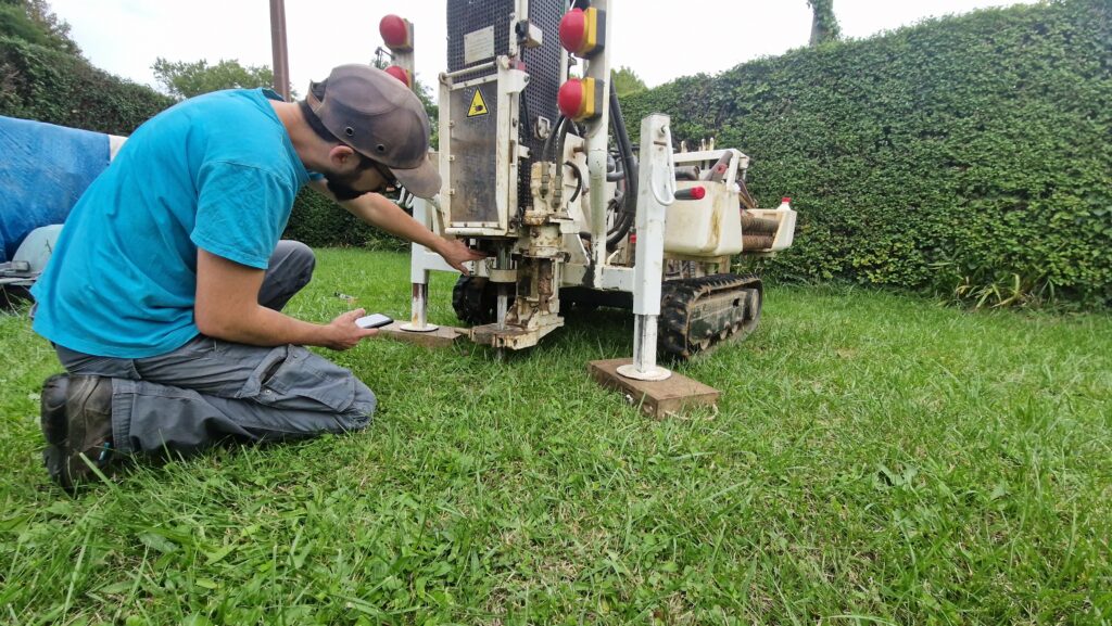 Technicien ajustant les paramètres d’une machine de forage lors d’une étude de sol en amont d’un projet immobilier, prestation dans le cadre de la garantie constructeur.