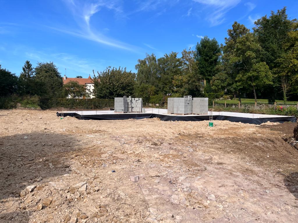 Terrain en construction avec fondations en béton pour une maison neuve. Préparation du sol et mise en place des premiers éléments de structure avant l’élévation des murs.