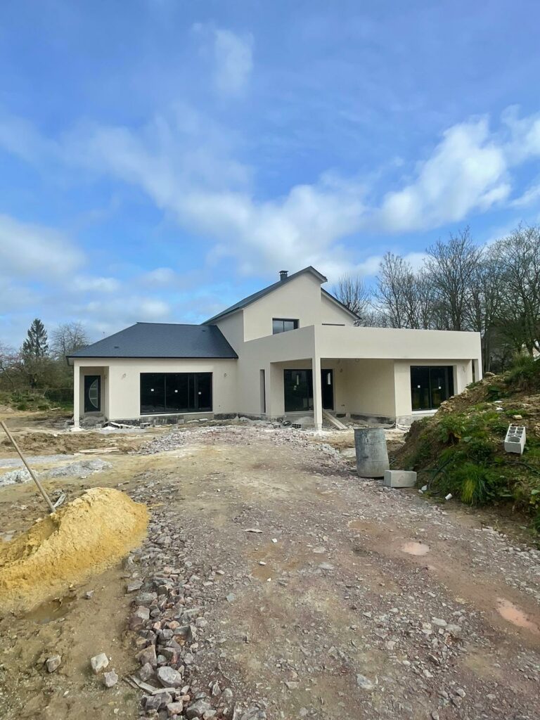 Maison moderne en phase de finition avec façade crépie et menuiseries installées. Construction avancée d’un projet architectural contemporain avec larges baies vitrées et toiture inclinée.